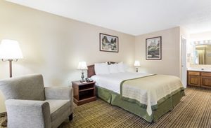 King bed and gray arm chair in hotel room at Baymont by Wyndham Greenwood